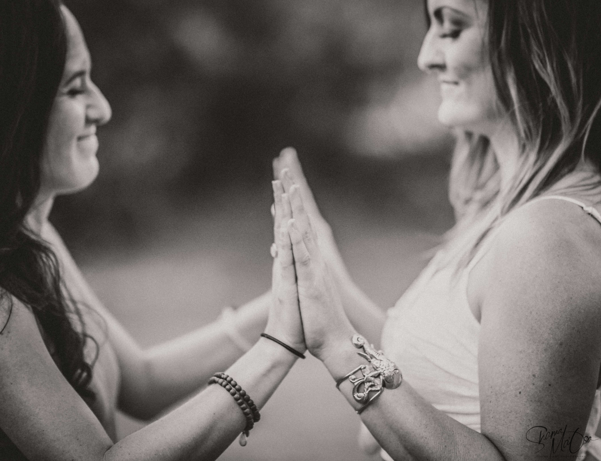 Two women facing one another with their palms pressed together