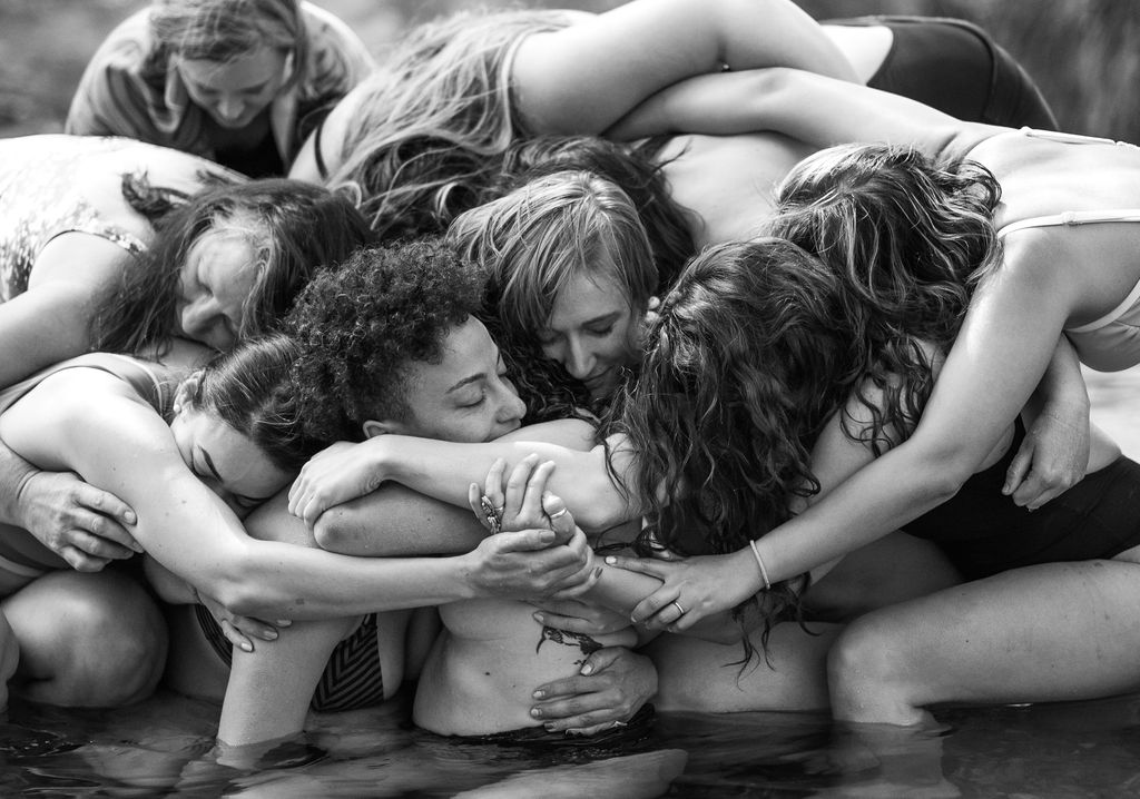 A group of women piled together, wrapped around and holding one another