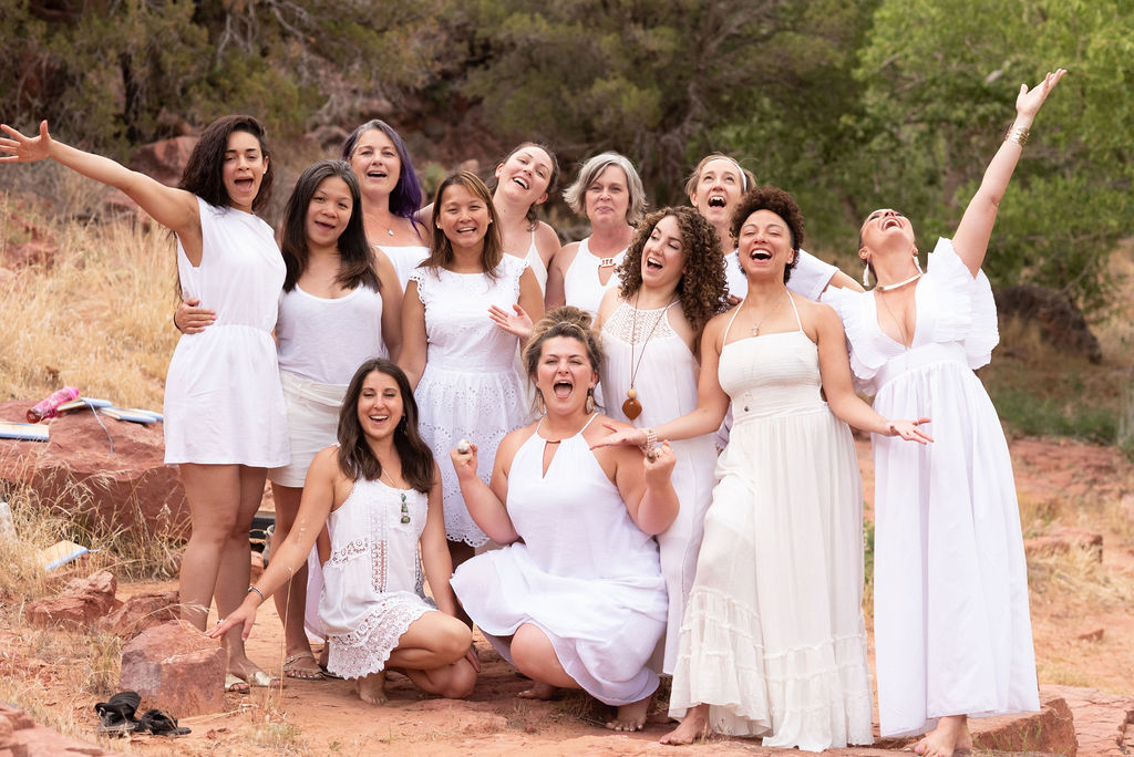 A circle of women in white on the red rocks, laughing together