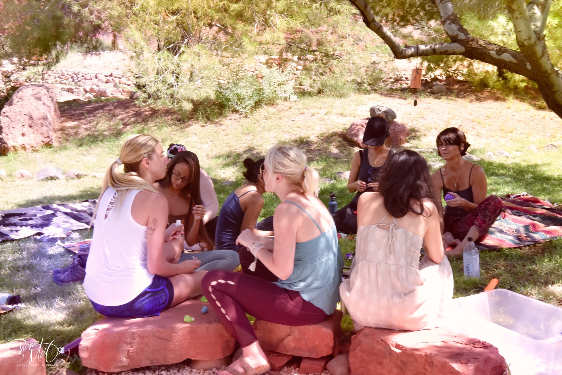 A group of women sitting together outside under the trees