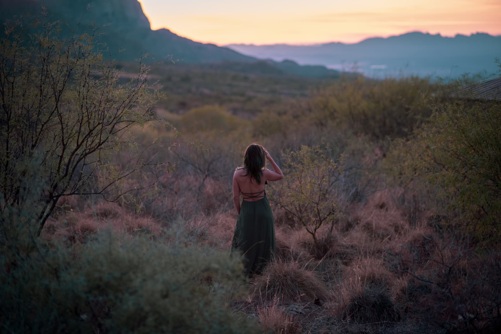 Woman walking through desert brush at sunset