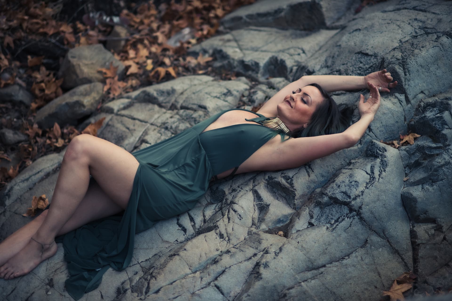 Jenna reclining across the rocks in a deep green dress